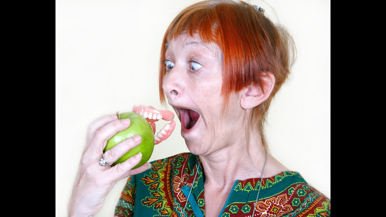 Woman with loose denture trying to bite an apple — limited eating struggle